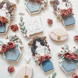 Könnte beinhalten: Dekorierte Zuckerkekse mit floralem Thema. Einige Kekse sind wie eine Frau mit Hut geformt, andere wie eine blaue Tasche mit Blumen, und einige sind oval mit einem goldenen Kettendesign. Ein Keks sagt "MAMA".