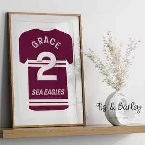 Könnte beinhalten: Ein druckbares Design mit einem maroonfarbenen Trikot mit weißem Text und einer weißen Nummer 2. Das Trikot trägt die Aufschrift "Grace" und "Sea Eagles".