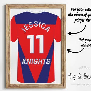 May include: A framed print of a red and blue sports jersey with the name "JESSICA" and the number "11" on the back. The jersey also has the word "KNIGHTS" printed on the bottom. The print is framed in a light brown wood frame.