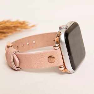 May include: A blush pink leather watch band with rose gold accents for an Apple Watch.