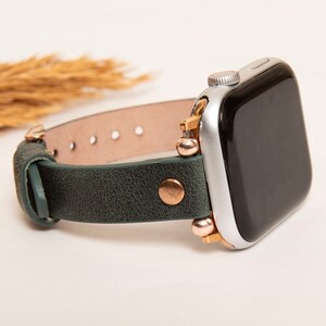 May include: A green leather watch band with rose gold accents and a silver Apple Watch.