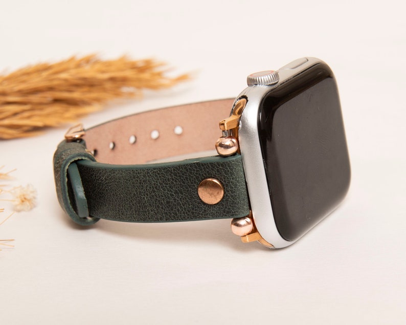 May include: A green leather watch band with rose gold accents and a silver Apple Watch.