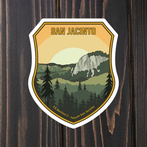 May include: A white sticker with a yellow, orange, and green mountain landscape. The text "SAN JACINTO" is at the top of the sticker. The text "CA Section C - Mount San Jacinto" is at the bottom of the sticker.