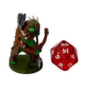 May include: A 3D-printed fantasy miniature of a green-skinned orc archer with a bow and quiver, standing on a green base. Beside it is a red twenty-sided die, commonly used in tabletop role-playing games. The orc is wearing brown armor.