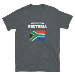 May include: Dark gray t-shirt featuring the text "PRETORIA" above a painted South African flag. The text "SOUTH AFRICA" is above the city name. The shirt is a short-sleeved crew neck.