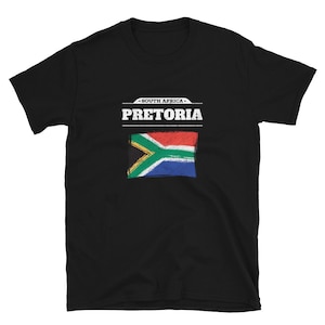 May include: Black t-shirt featuring the text "PRETORIA" above a distressed South African flag design. The text "SOUTH AFRICA" is above the city name. The shirt is a short-sleeved crew neck.