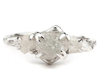 May include: A silver-toned ring featuring three raw, uncut, translucent white stones set in metal prongs. The band has a textured, organic appearance resembling tree bark, with a central larger stone flanked by two smaller stones on each side.