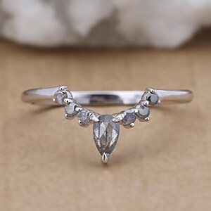 May include: A silver ring with a curved design, featuring a central pear-shaped gray stone and smaller round gray stones. The ring's band is thin and polished, with a delicate, elegant appearance.