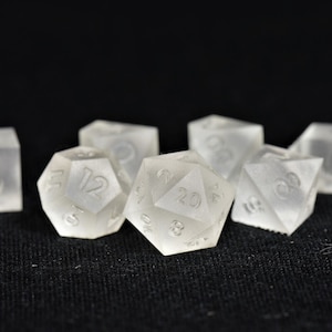 May include: A set of six clear, frosted dice with black numbers. The dice are in various shapes and sizes, including a 20-sided die, a 12-sided die, and a 6-sided die.