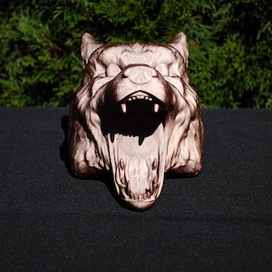 May include: A detailed, carved wooden sculpture of a wolf's head with an open mouth, showing sharp teeth. The sculpture is painted in shades of brown and white.
