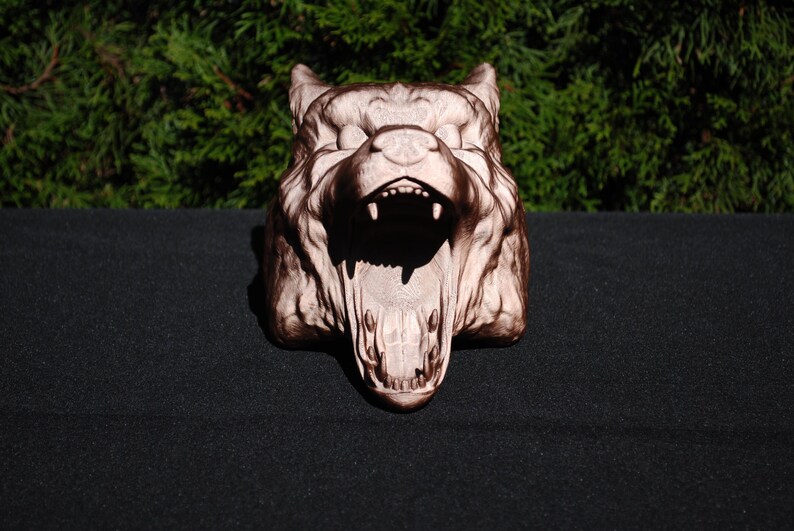 May include: A detailed, carved wooden sculpture of a wolf's head with an open mouth, showing sharp teeth. The sculpture is painted in shades of brown and white.