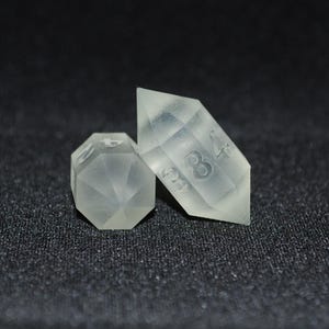 May include: Two clear, translucent dice with numbers etched on their faces. The dice are shaped like a pyramid and a diamond. The pyramid die has the number 8 on one face and the diamond die has the number 4 on one face.