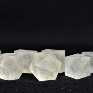 May include: A set of six translucent white dice with black numbers. The dice are in various shapes, including a 20-sided die, a 12-sided die, and a 6-sided die.