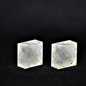 May include: Two white opaque dice with intricate designs on each face. The dice are sitting on a black surface.