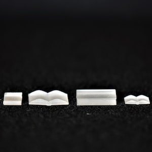 May include: Four white plastic bookends of varying sizes, arranged in a row on a black surface.