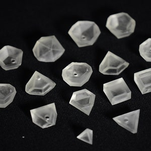 Pode incluir: Uma coleção de 15 formas geométricas de plástico transparente, incluindo um cubo, uma pirâmide, um diamante e outros poliedros. As formas são todas translúcidas e têm um acabamento liso e polido.