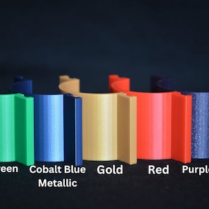 May include: Six different colored plastic rings, from left to right: light green, cobalt blue metallic, gold, red, purple sparkle, and black.