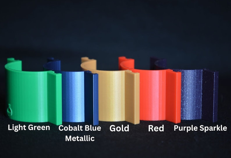 May include: Six different colored plastic rings, from left to right: light green, cobalt blue metallic, gold, red, purple sparkle, and black.