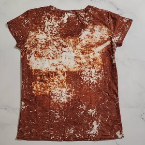 Puede incluir: Una camiseta de manga corta con cuello en V con un dise&ntilde;o blanqueado marr&oacute;n y blanco. La camiseta tiene un aspecto texturizado y un estilo casual. El patr&oacute;n blanqueado crea un aspecto &uacute;nico y art&iacute;stico, adecuado para el uso diario.