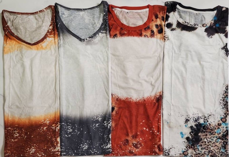 Puede incluir: Cuatro camisetas blancas con dise&ntilde;os &uacute;nicos. La primera tiene un efecto degradado marr&oacute;n y naranja, la segunda un degradado gris y blanco, la tercera un dise&ntilde;o rojo y estampado de leopardo, y la cuarta un patr&oacute;n en blanco y negro.