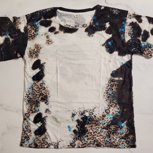 Puede incluir: Camiseta blanca con un patr&oacute;n &uacute;nico que presenta formas abstractas negras, marrones y azules. El dise&ntilde;o incluye detalles de estampado de leopardo y un cuello negro. Una camiseta casual de manga corta.