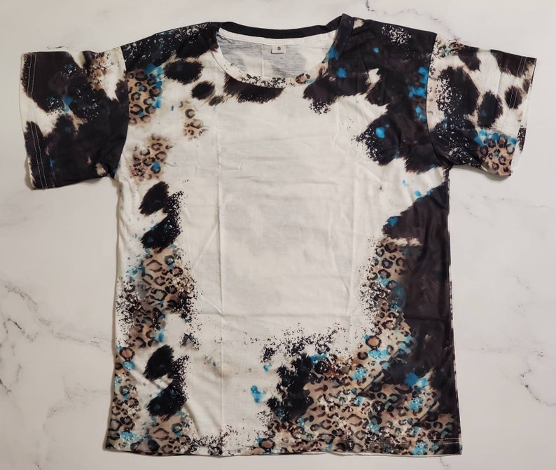 Puede incluir: Camiseta blanca con un patr&oacute;n &uacute;nico que presenta formas abstractas negras, marrones y azules. El dise&ntilde;o incluye detalles de estampado de leopardo y un cuello negro. Una camiseta casual de manga corta.