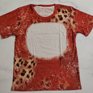 Puede incluir: Una camiseta de manga corta con un dise&ntilde;o &uacute;nico. La camiseta presenta un esquema de color rojo y blanco con un estampado de leopardo y un gran c&iacute;rculo blanco en el centro. Tiene cuello redondo.