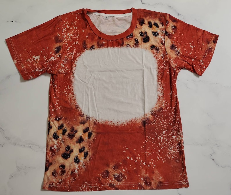Puede incluir: Una camiseta de manga corta con un dise&ntilde;o &uacute;nico. La camiseta presenta un esquema de color rojo y blanco con un estampado de leopardo y un gran c&iacute;rculo blanco en el centro. Tiene cuello redondo.