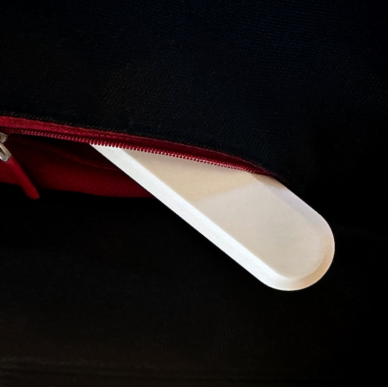 May include: A white rectangular object is partially visible inside a red zippered pocket of a black bag.