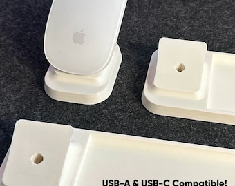 Puede incluir: Soporte de plástico blanco con dos ranuras para un ratón y un teléfono. El soporte tiene un agujero para cables de carga. El texto "USB-A & USB-C Compatible! Múltiples colores disponibles!" está impreso en el soporte.