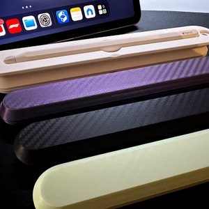 May include: Four cases for an Apple Pencil. The cases are made of different materials, including a white case with the text "Apple Pencil", a black case with a carbon fiber pattern, a purple case with a carbon fiber pattern, and a white case.