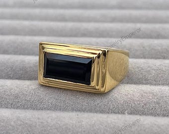 May include: A gold ring featuring a black rectangular gemstone. The ring has a simple design with a smooth band and a raised setting for the stone.