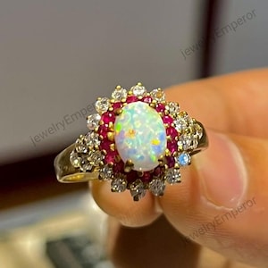 Può includere: Un anello d'oro con una grande opale ovale circondata da un'aureola di piccoli rubini rossi e diamanti bianchi.