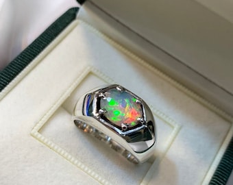 May include: A silver ring with a large, multi-colored opal gemstone set in a hexagonal bezel. The ring is displayed in a green velvet ring box.