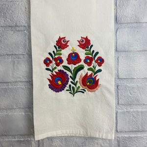 May include: White kitchen towel with a red, blue, green, and yellow embroidered floral design.