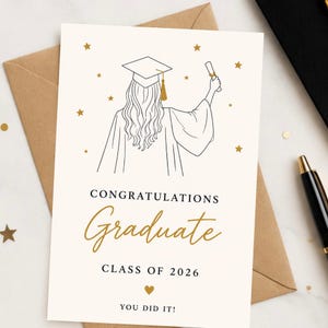 Puede incluir: Tarjeta de graduación con un dibujo lineal de una graduada con birrete y toga, sosteniendo un diploma. La tarjeta tiene las palabras "Congratulations Graduate Class of 2026 You Did It!" en oro y negro.