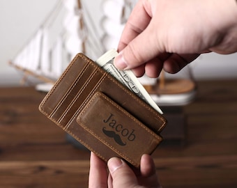 May include: A brown leather wallet with a money clip and a personalized inscription that reads "Jacob" with a mustache graphic.