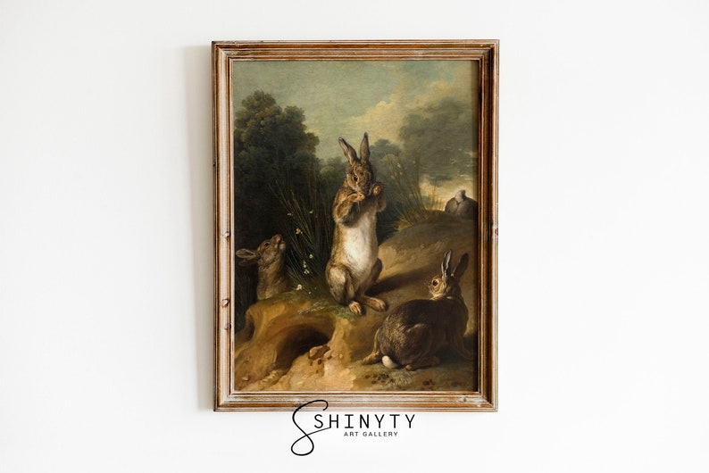 May include: A framed oil painting depicting three rabbits in a woodland setting. The rabbits are brown and white, and they are standing and sitting in a grassy area. The painting is set against a backdrop of trees and a cloudy sky.