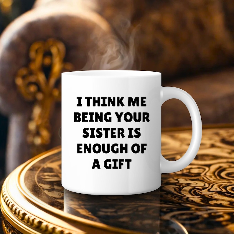 May include: A white ceramic mug with the text "I THINK ME BEING YOUR SISTER IS ENOUGH OF A GIFT" in black. The mug has a curved handle and is filled with a hot beverage, with steam rising from the top. The mug is on a decorative table.
