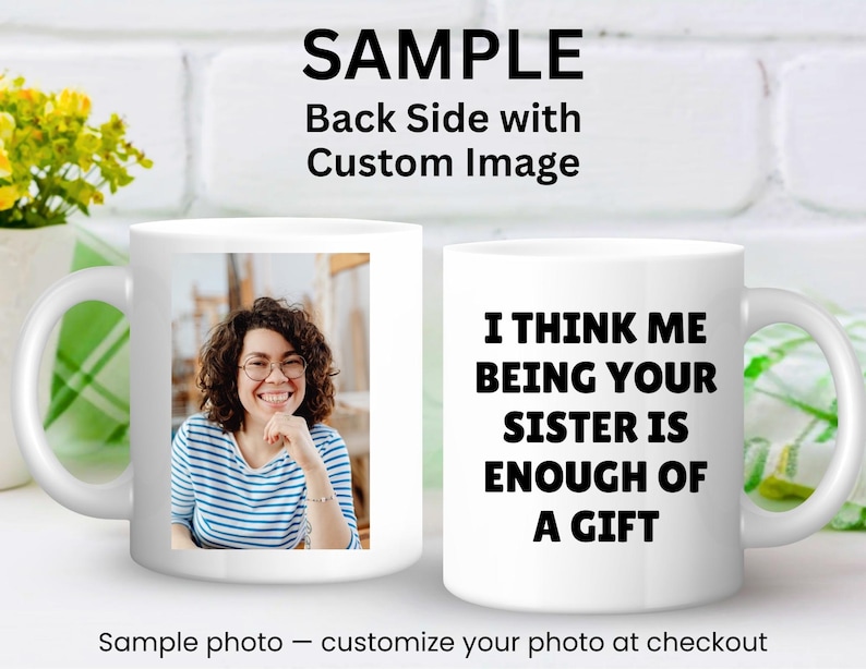 May include: White ceramic mug featuring a photo of a smiling person on one side and the text "I THINK ME BEING YOUR SISTER IS ENOUGH OF A GIFT" on the other. The mug has a curved handle and is set against a white brick background.