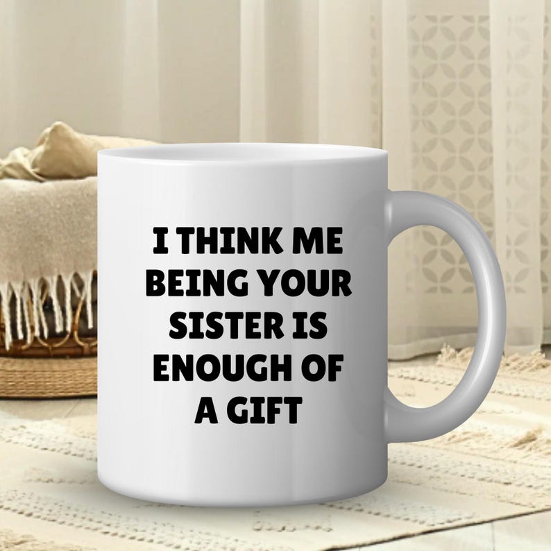 May include: White ceramic mug with a curved handle. The mug features the text "I THINK ME BEING YOUR SISTER IS ENOUGH OF A GIFT" in black, centered on the front. The mug is on a patterned rug.