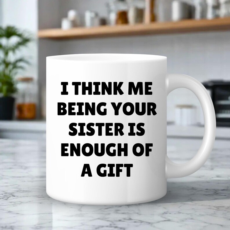 May include: White ceramic mug with a curved handle. The mug features the black text: "I THINK ME BEING YOUR SISTER IS ENOUGH OF A GIFT". The mug is on a marble surface.