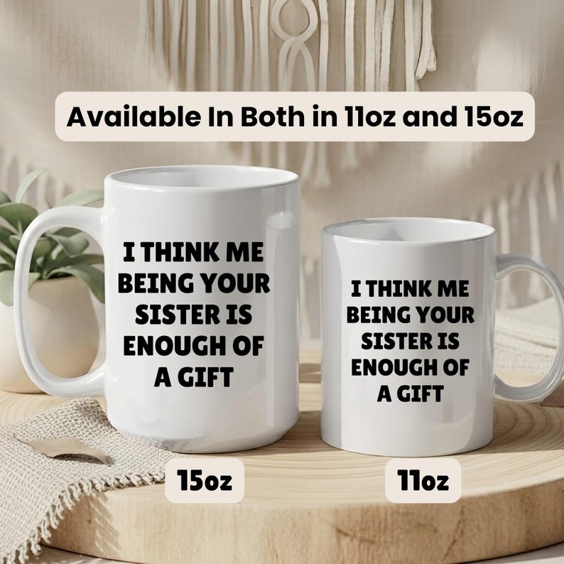 May include: Two white ceramic mugs with black text that reads "I THINK ME BEING YOUR SISTER IS ENOUGH OF A GIFT." The mugs are labeled 15oz and 11oz. The text "Available In Both in 11oz and 15oz" is above the mugs.