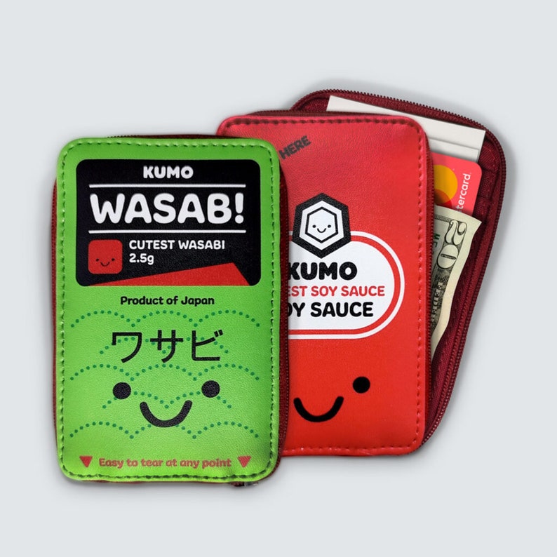 May include: A green and red zippered pouch with a cartoon design. The pouch has a zipper closure and is made of a soft, textured material. The front of the pouch features a cartoon image of a wasabi packet with the text "KUMO WASAB! CUTEST WASABI 2.5g Product of Japan ワサビ". The back of the pouch features a cartoon image of a soy sauce packet with the text "KUMO EST SOY SAUCE OY SAUCE".