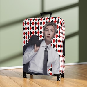 May include: A rectangular upright suitcase featuring a repeating red, white, and black diamond harlequin pattern. The front displays a photographic print of a person with short light brown hair wearing a white dress shirt and a dark tie.