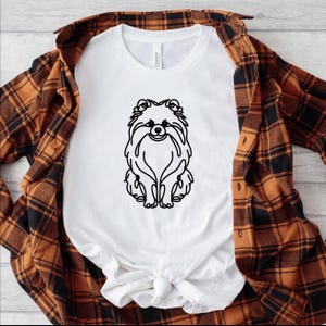 May include: White t-shirt with a black line drawing of a Pomeranian dog on the front.