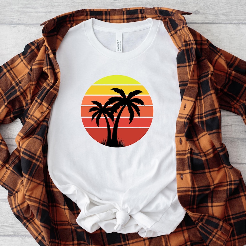 May include: White t-shirt with a retro sunset graphic featuring two palm trees. The sunset is in shades of yellow, orange, and red.