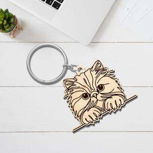 May include: A wooden keychain featuring a Persian cat design. The cat's face is intricately carved with detailed fur and large eyes. The keychain includes a silver-colored metal ring for attaching keys.
