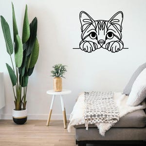May include: A black and white cat wall art decal. The cat's head and paws are visible, peeking over a horizontal line. The cat's face has detailed line art, with large eyes and a striped pattern.