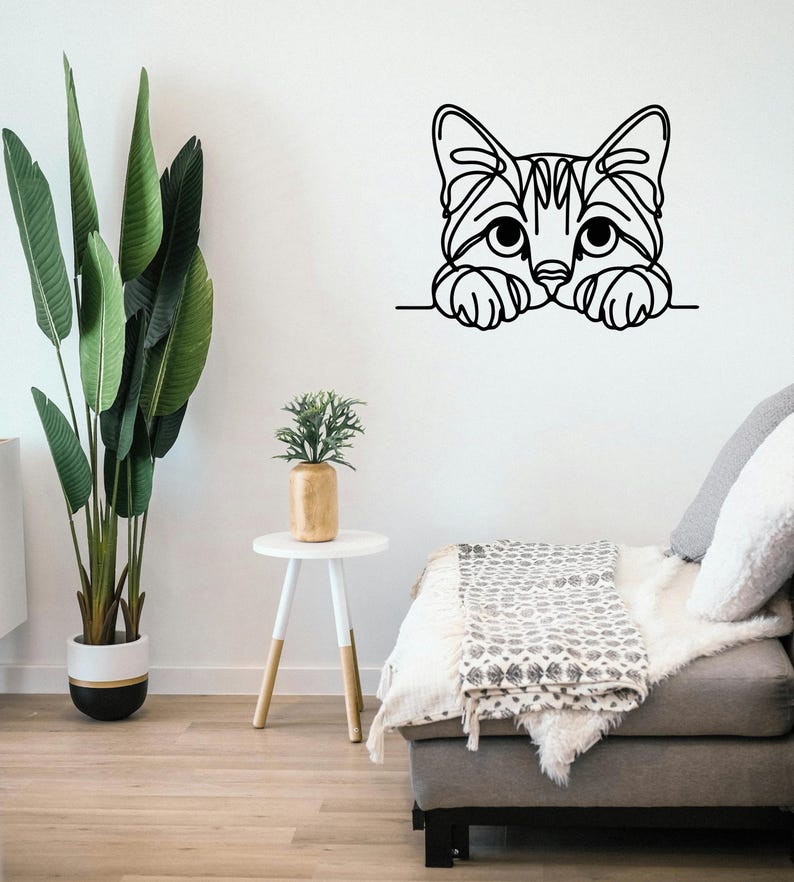 May include: A black and white cat wall art decal. The cat's head and paws are visible, peeking over a horizontal line. The cat's face has detailed line art, with large eyes and a striped pattern.